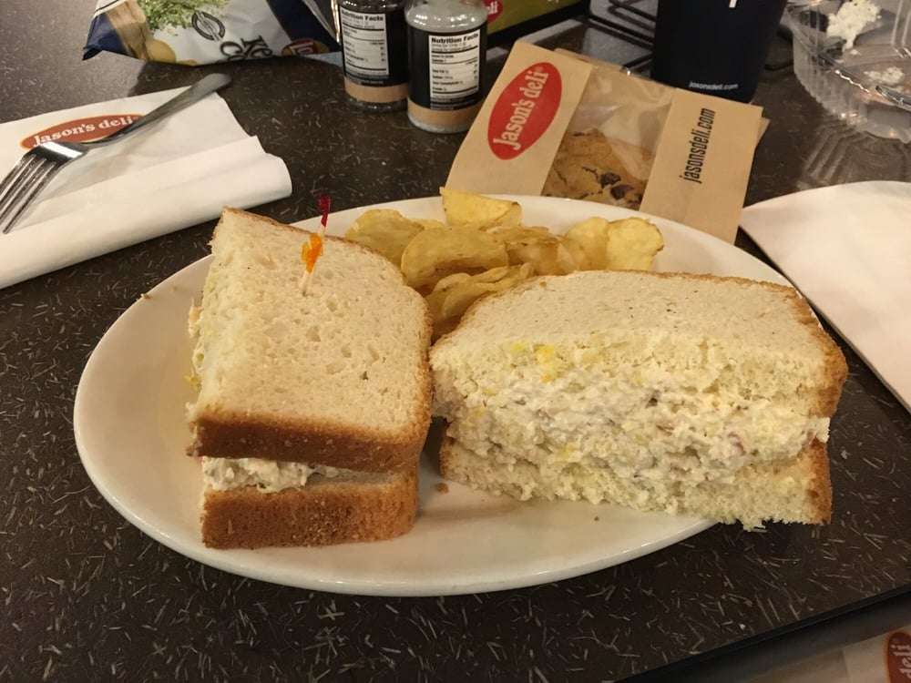 Chicken salad sandwich on white bread with kettle chips and a couple ...